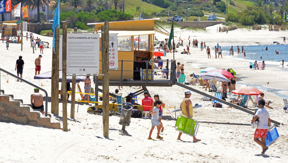 Caseta de guardavidas de una playa. A lo largo, se ven varias personas tomando sol en la arena